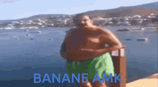 a shirtless man in green shorts is standing in front of a body of water with the words " bananae amk " on the bottom