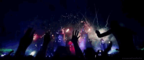 a crowd at a concert with their hands in the air watching fireworks