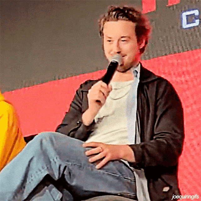 a man in a black jacket is holding a microphone in his mouth while sitting down