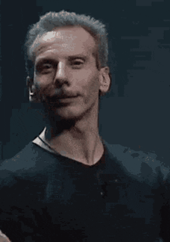 a man in a black shirt is smiling and waving his hand in the dark .