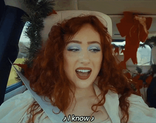 a woman with red hair is sitting in the back seat of a car and says i know