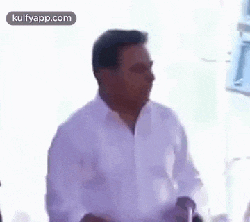 a man in a white shirt is standing in front of a white wall and making a funny face .