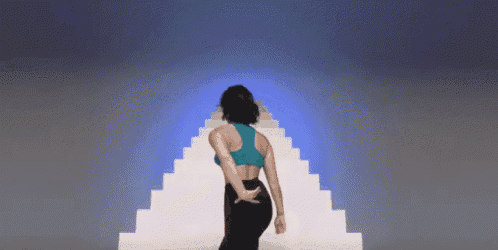 a woman in a blue top and black pants is standing in front of a staircase .