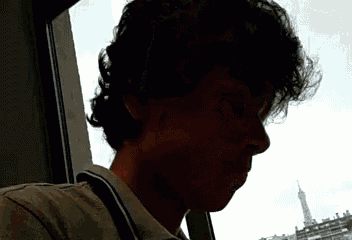 a man with curly hair looking out a window