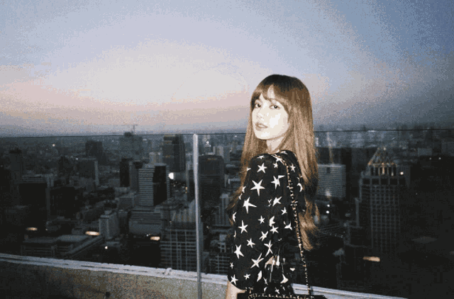 a woman in a black and white star print dress stands on a balcony overlooking a city
