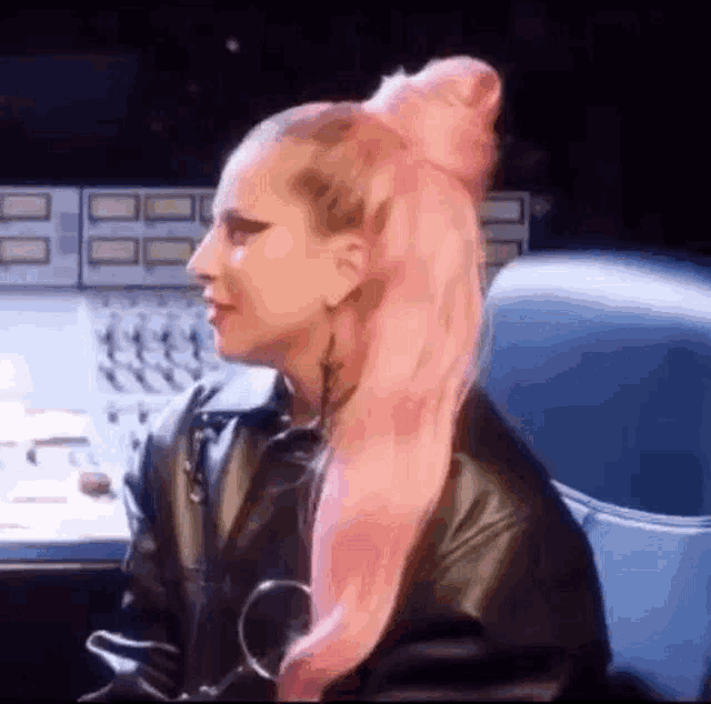 a woman with pink hair is wearing a leather jacket and sitting in a chair .