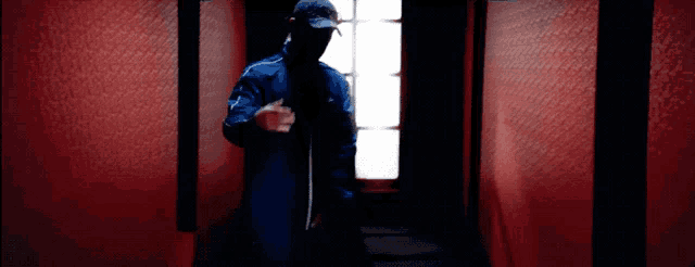 a man in a blue jacket and black hat stands in a dark hallway