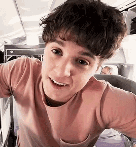 a young man in a pink t-shirt is taking a selfie on an airplane .