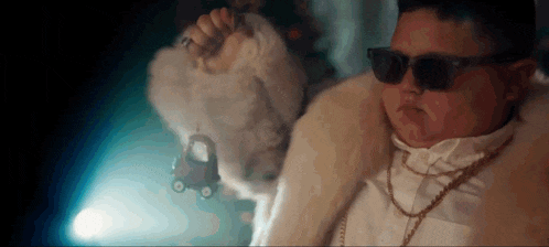 a man in a fur coat and sunglasses is holding a toy car in his hand .