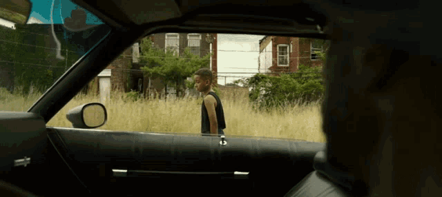 a boy in a black tank top is standing in a grassy field