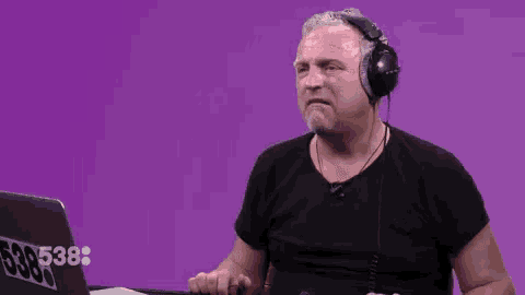 a man wearing headphones is sitting in front of a laptop on a purple background .