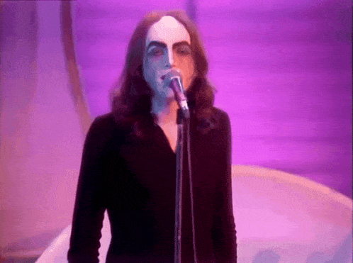 a man with long hair singing into a microphone with his face painted