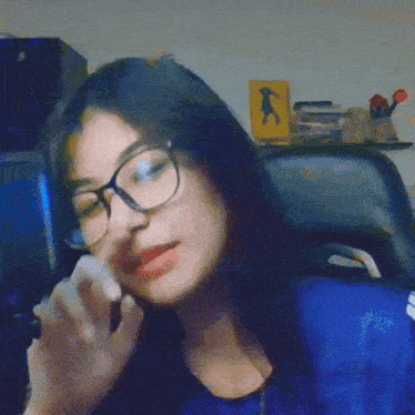 a woman wearing glasses is sitting in a chair in front of a yellow sign that says ' a ' on it