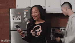a man and a woman are standing in a kitchen looking at their cell phones ..