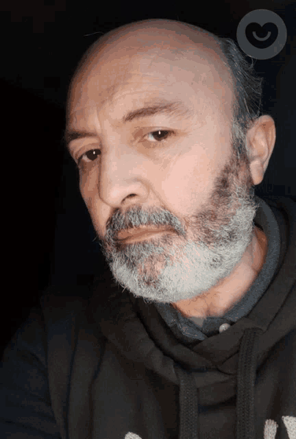a man with a beard is wearing a black hoodie with a heart in the background