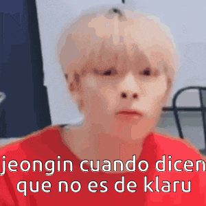 a man with blonde hair is wearing a red shirt and making a funny face while talking in spanish .