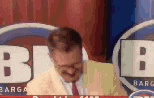 a man in a suit and tie is sitting in front of a sign that says barg
