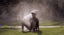 a man is sitting on the grass in front of a sprinkler .