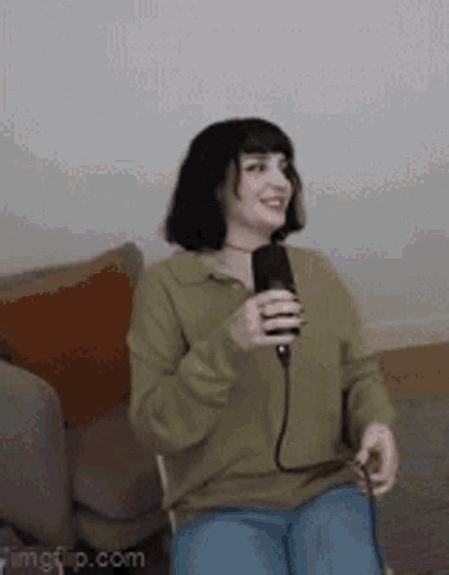 a woman is sitting on a chair holding a microphone and smiling .