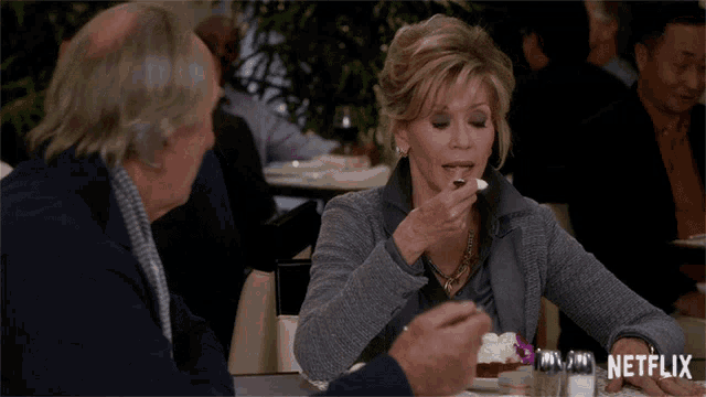 a woman is sitting at a table with a glass of netflix in the background