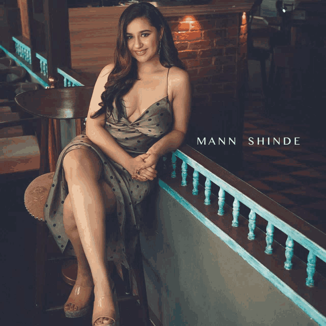a woman in a polka dot dress leans on a railing with mann shinde written on the bottom right