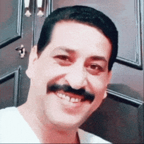 a man with a mustache is smiling in front of a wooden door
