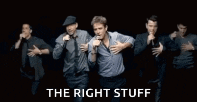 a group of men are standing next to each other singing into microphones on a stage .