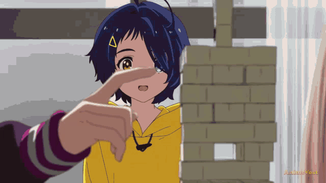 a girl in a yellow hoodie is pointing at a stack of bricks