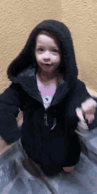 a little girl is wearing a black jacket with a hood
