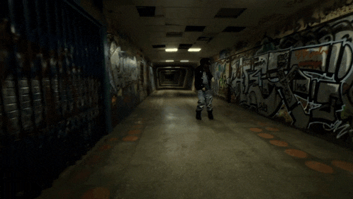 a person standing in a dark hallway with graffiti on the wall