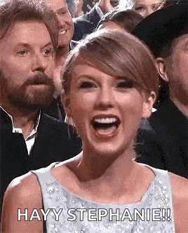 taylor swift is laughing while sitting in a crowd of people at an event .