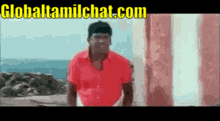 a man in a red shirt is standing in front of a striped wall with the website globaltamilchat.com written on the bottom