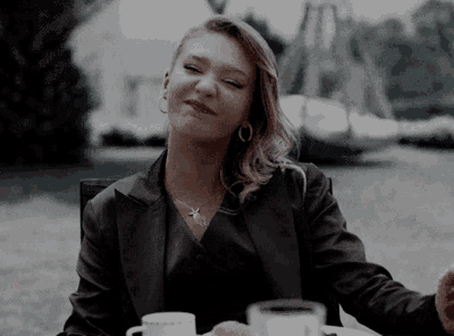a woman is sitting at a table with two cups of coffee