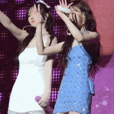 a woman in a blue dress stands next to a woman in a white dress on a stage