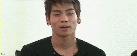 a young man wearing a black shirt and a necklace is looking at the camera .