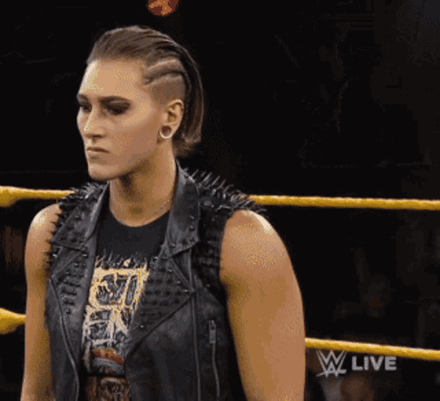 a woman in a leather vest is standing in a wrestling ring with the words w live on the bottom