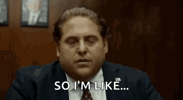 a man in a suit and tie is saying `` so i 'm like '' while sitting at a desk .