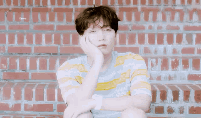 a young boy is sitting in front of a brick wall with his hand on his face .