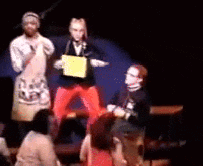 a group of people are standing on a stage with a man holding a yellow box