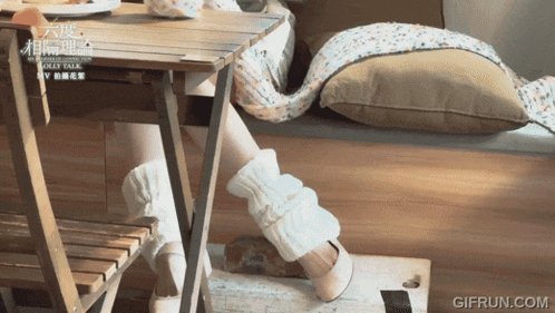 a woman wearing leg warmers sits at a table with a gifrun.com watermark