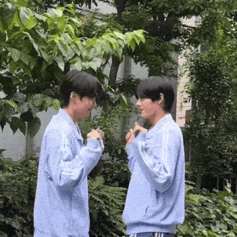 two young men in blue jackets are standing next to each other in a park .