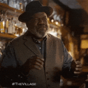 an older man wearing a hat and vest is standing in a bar .