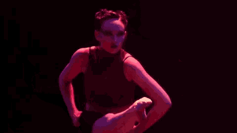 a woman in a black top is doing a split in a dark room