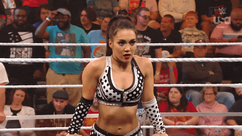 a female wrestler in a polka dot outfit stands in a wrestling ring with a crowd watching