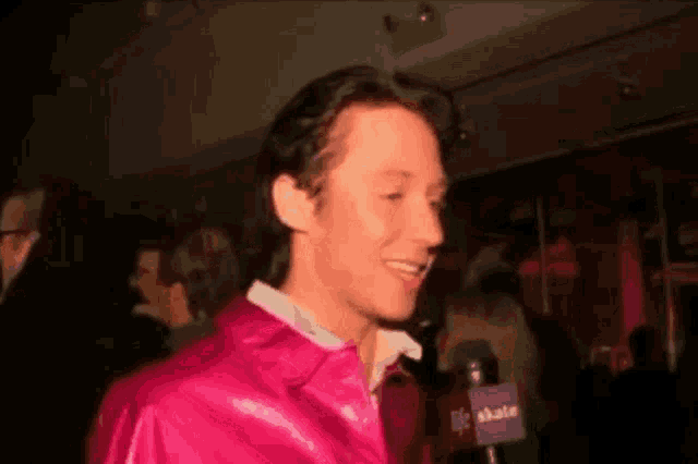 a man wearing a pink jacket is talking into a microphone with the word life on it