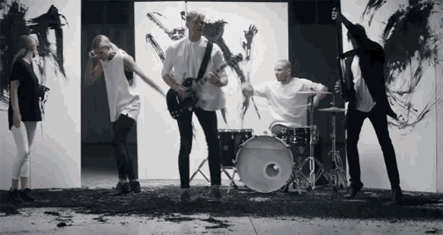 a group of people standing around a drum set in front of a wall