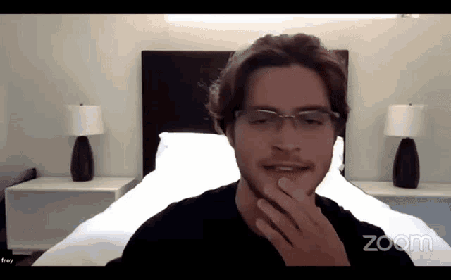 a man wearing glasses is on a zoom call with a bedroom in the background