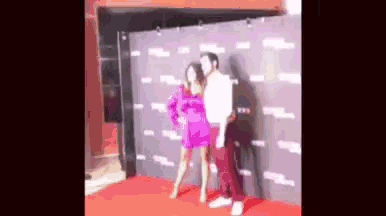 a man and a woman are posing for a picture on a red carpet . the woman is wearing a pink dress .