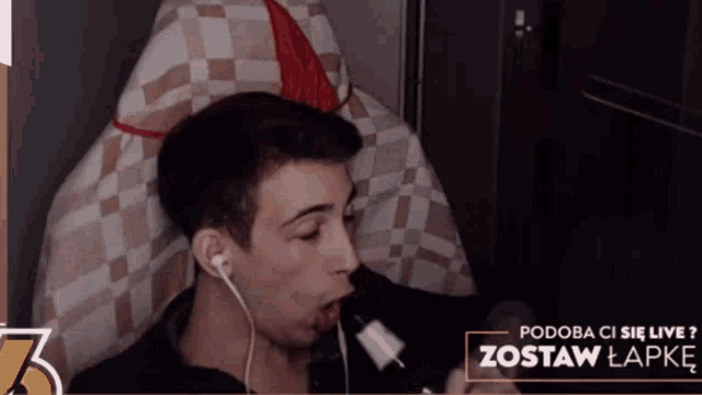 a man wearing ear buds is sitting in front of a sign that says " zestaw lapke "