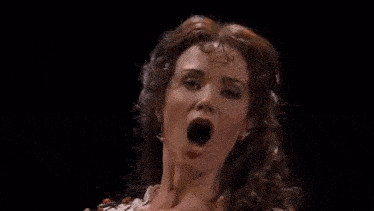 a woman is singing into a microphone on a stage in front of a black background .